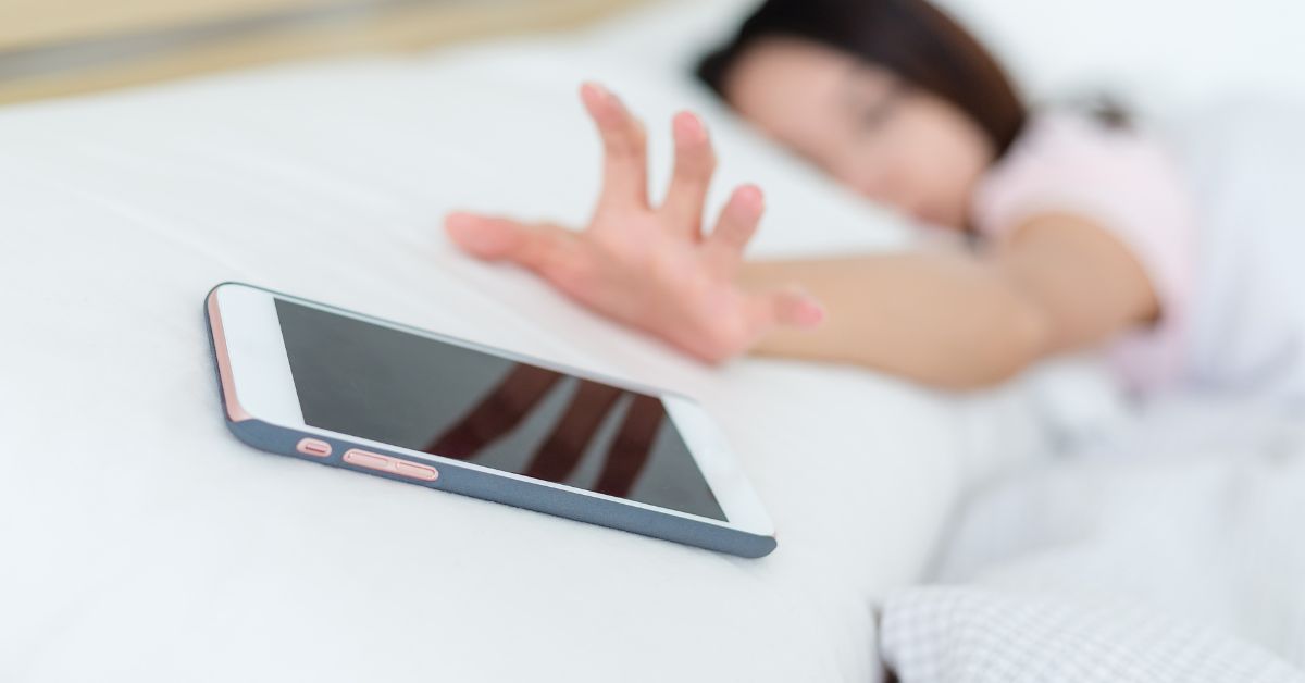 woman reaching for phone in bed