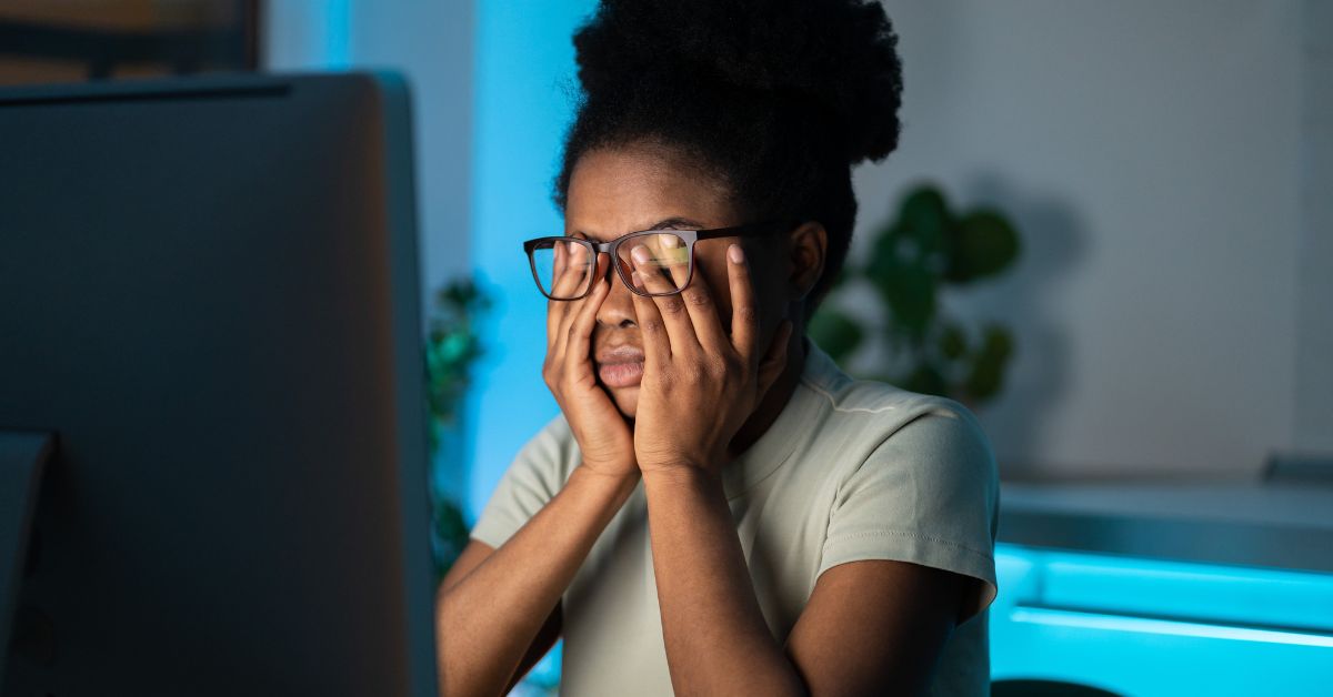 woman in front of a computer rubbing her eyes feeling the affects of eye strain from too much screen time