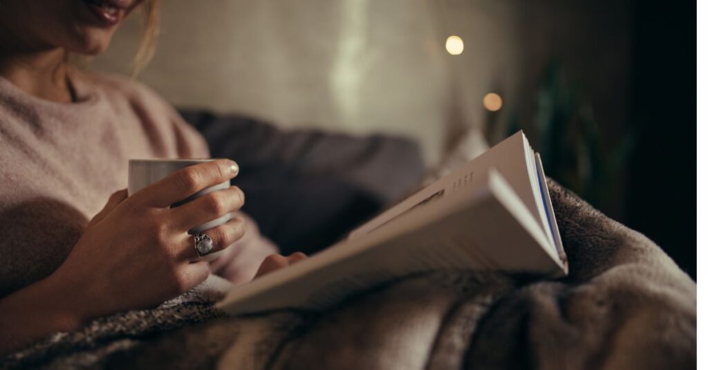 women with a blanket and book, cup of coffee, unwinding from screen time to create some digital boundaries in her life