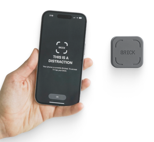 A picture of the square Brick device and an iPhone beside it with the words "This is a distraction" on the screen demonstrating that when you Brick your phone, it blocks the apps you set to block.