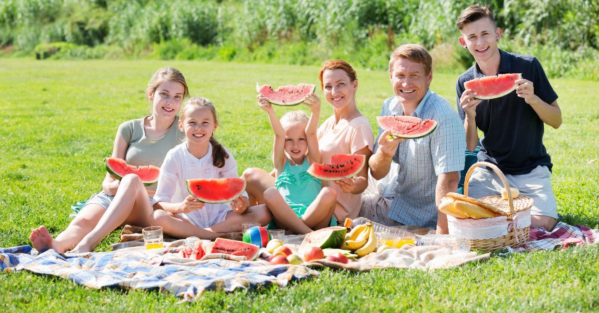 A family of 6 eating watermelon in park demonstrating time without screens is fun and healthy