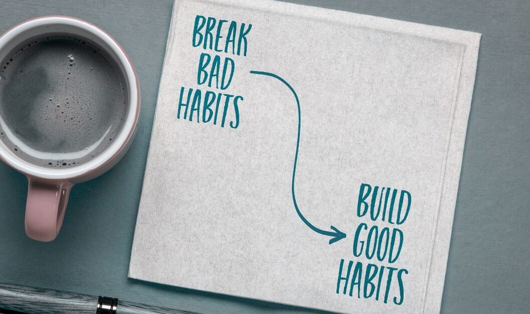 An arial picture of a coffee mug and pen with an open book that says "break bad habits" with a curvy arrow pointing to the words "build good habits"