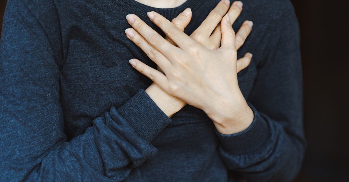 a woman wearing a grey sweater with her hands over her heart inferring her care for her heart. You cannot see her face.