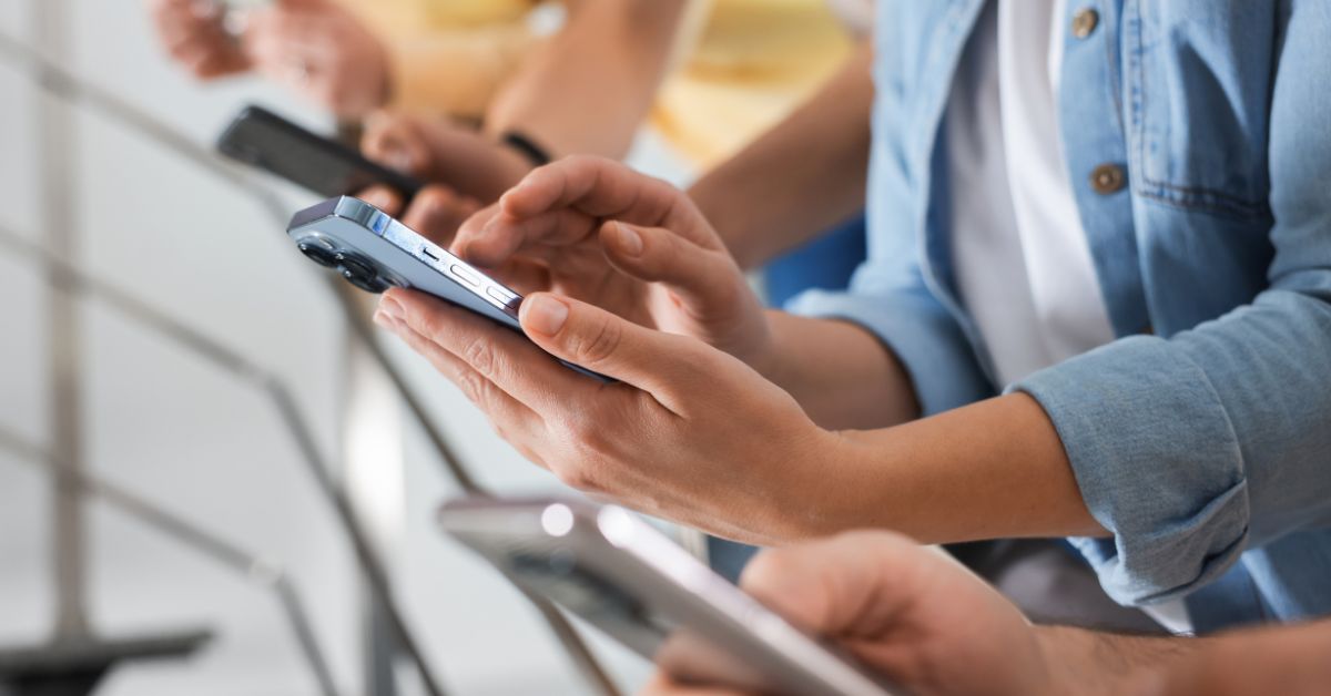 Close up of several people standing side by side using their smartphones with focused attention on their screens, suggesting constant device use in a shared space. The scene highlights everyday behavior linked to phone addiction and the challenge to break phone addiction in social settings.