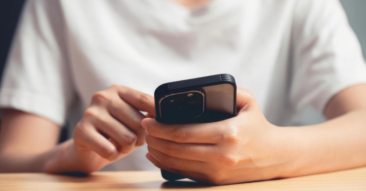 A person holds a smartphone at a table with their finger ready to scroll. The close up view highlights how phone scrolling can interrupt deep focus and shape attention habits over time.