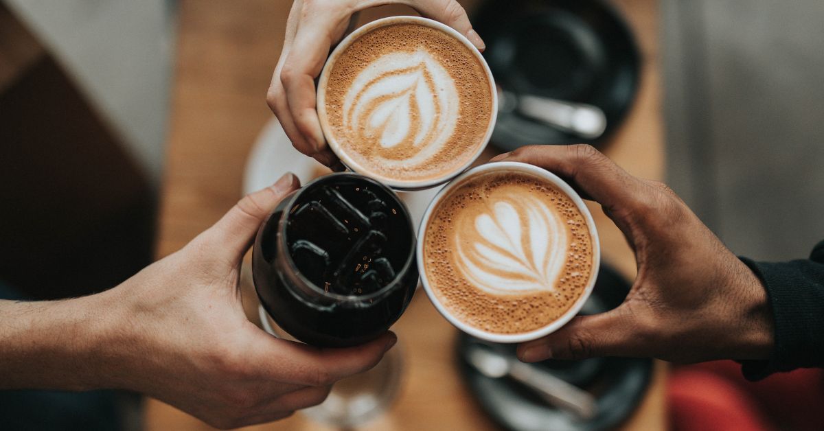 Three people hold coffee drinks close together around a table during a shared moment. The scene supports a blog post about phone free time and being fully present with the people you love.
